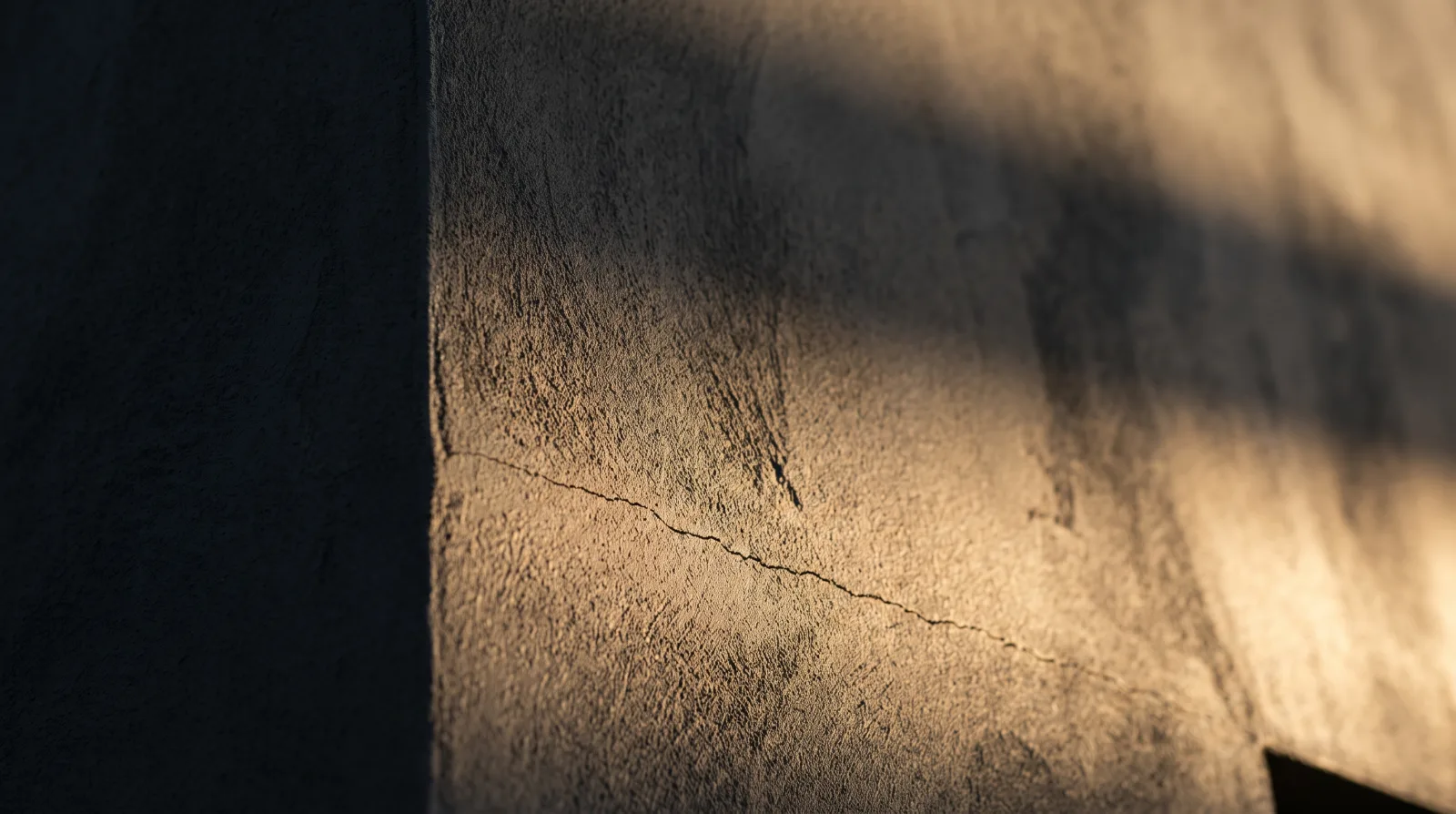Close-up of a stucco wall corner showing a hairline crack in warm raking light