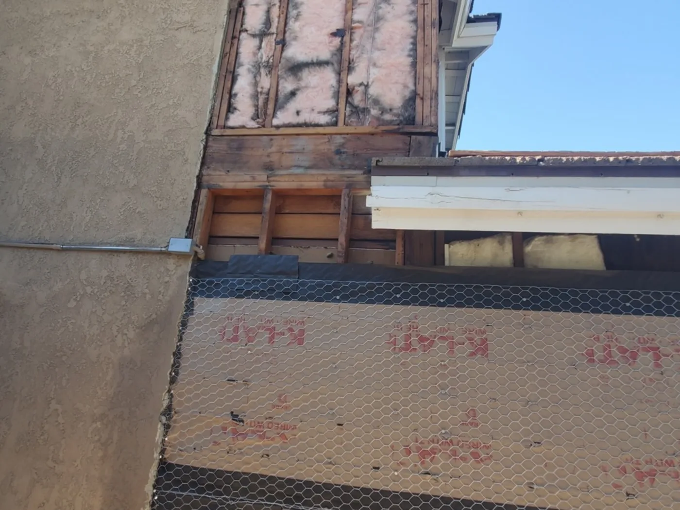 Before: House exterior stripped to wire lath and framing before stucco
